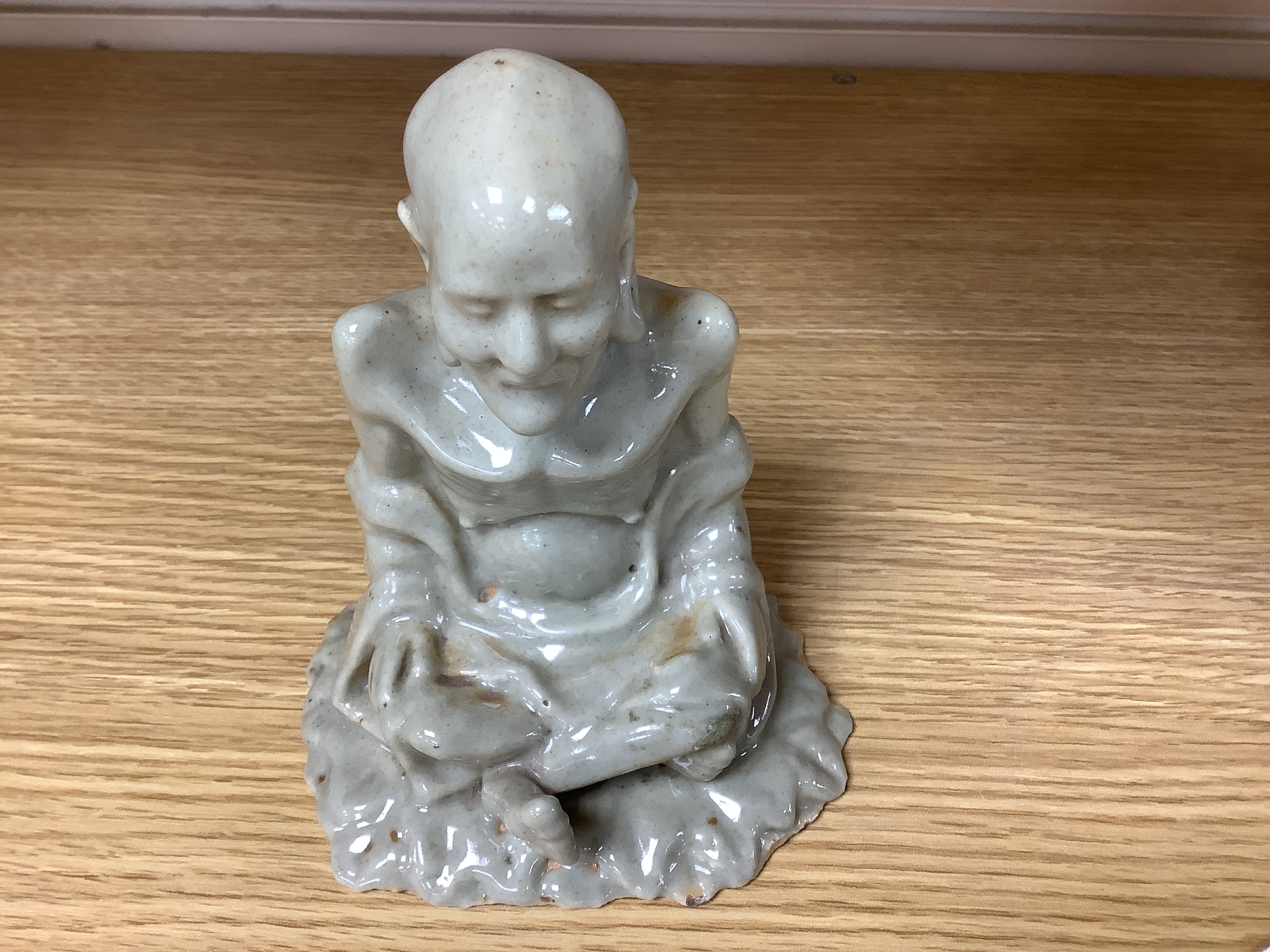 A Chinese celadon glazed figure of Laozi, 18th / 19th century, cross-legged and seated on leaves, 15cm high